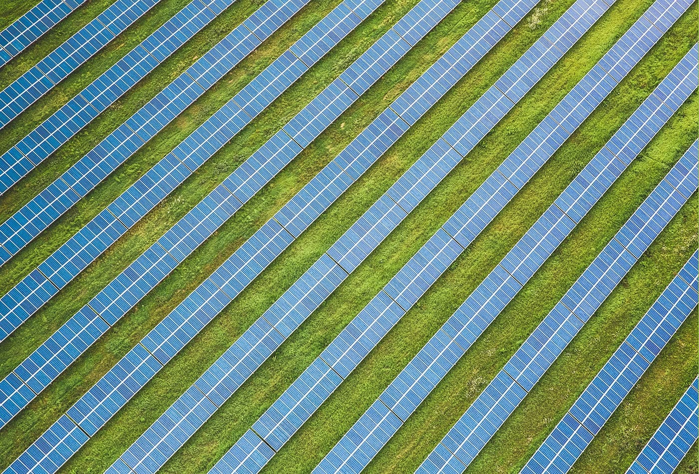 Rows Of Solar Panels Line Up In Perfect Symmetry, Harnessing The Sun'S Energy Amidst A Field Of Green.